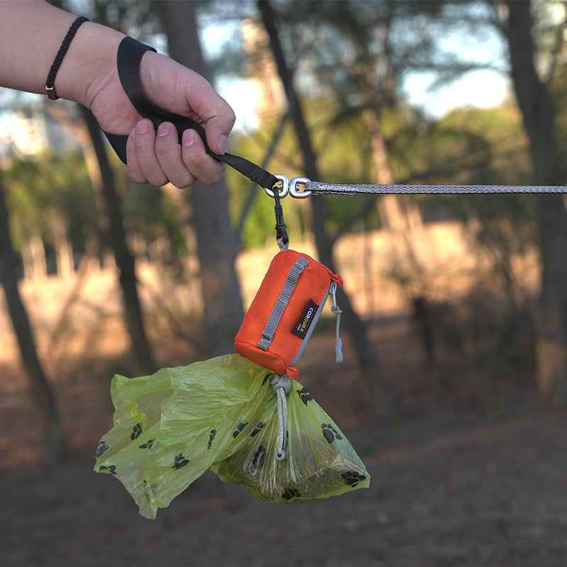 Person holding a leash with a poop bag dispenser attached, outdoors.