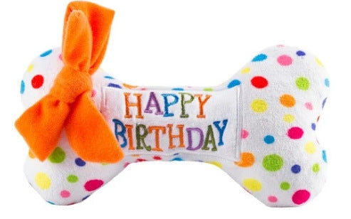 Polka dot bone-shaped toy with 'Happy Birthday' text and orange bow on a white background