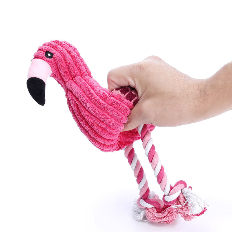 Pink flamingo-shaped dog toy with a rope, held by a hand against a white background