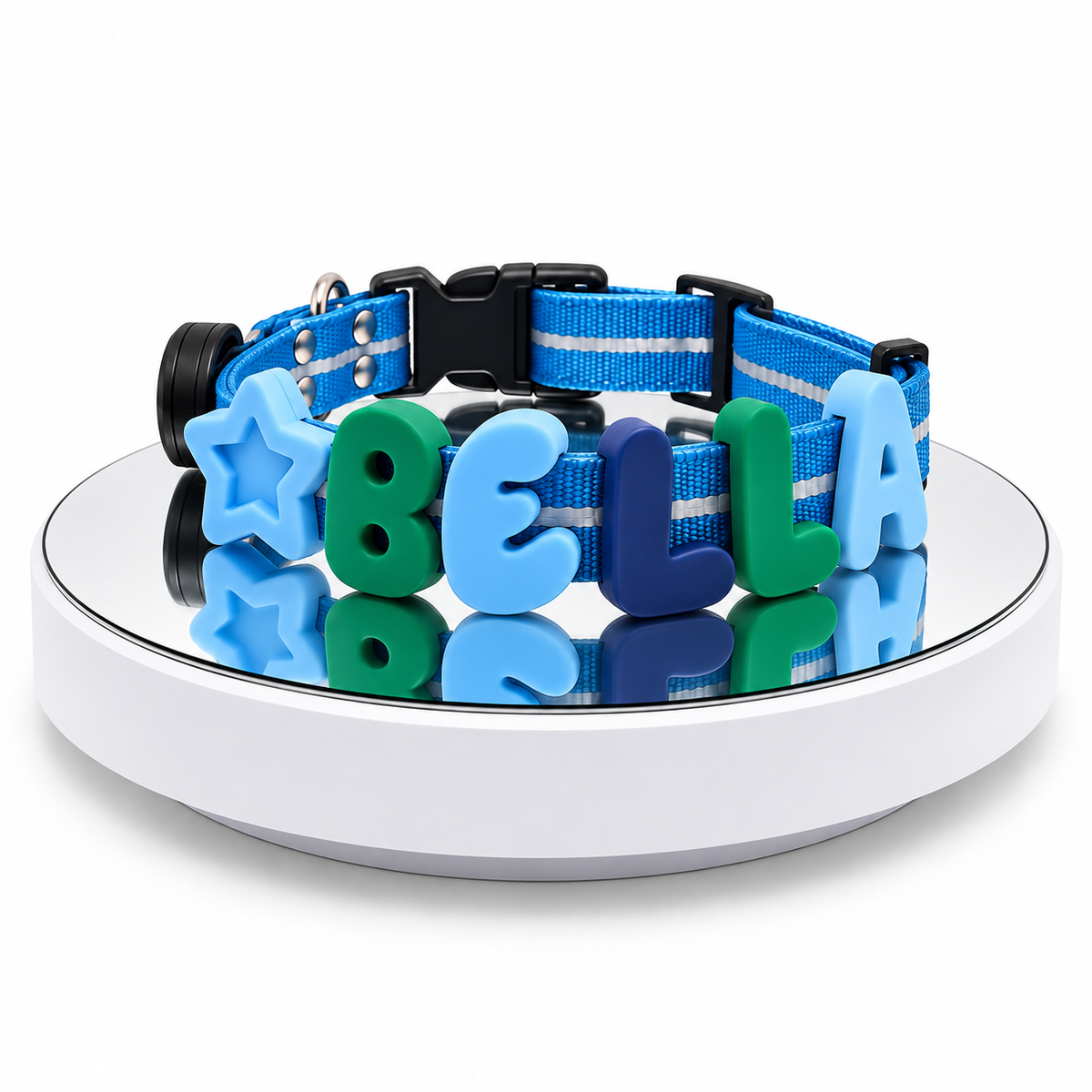 A blue dog collar with black plastic hardware and colorful letter charms spelling 'BELLA' and a star, displayed on a white circular stand against a white background.
