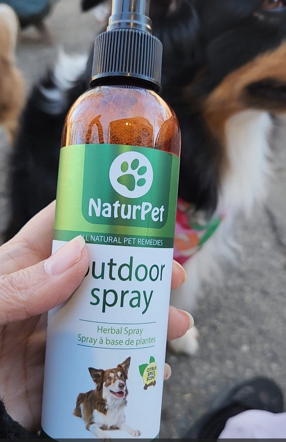 NaturPet outdoor spray bottle held by a person with a dog in the background