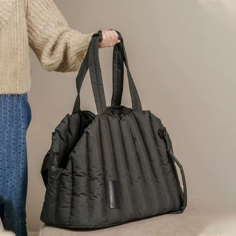 Person holding a black duffel bag against a neutral background