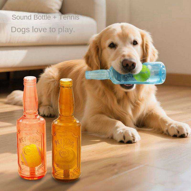 A golden retriever lies on a wooden floor in a living room, holding a translucent blue bottle-shaped toy in its mouth. Two bottle-shaped sound toys, one pink and one amber, sit in the foreground.